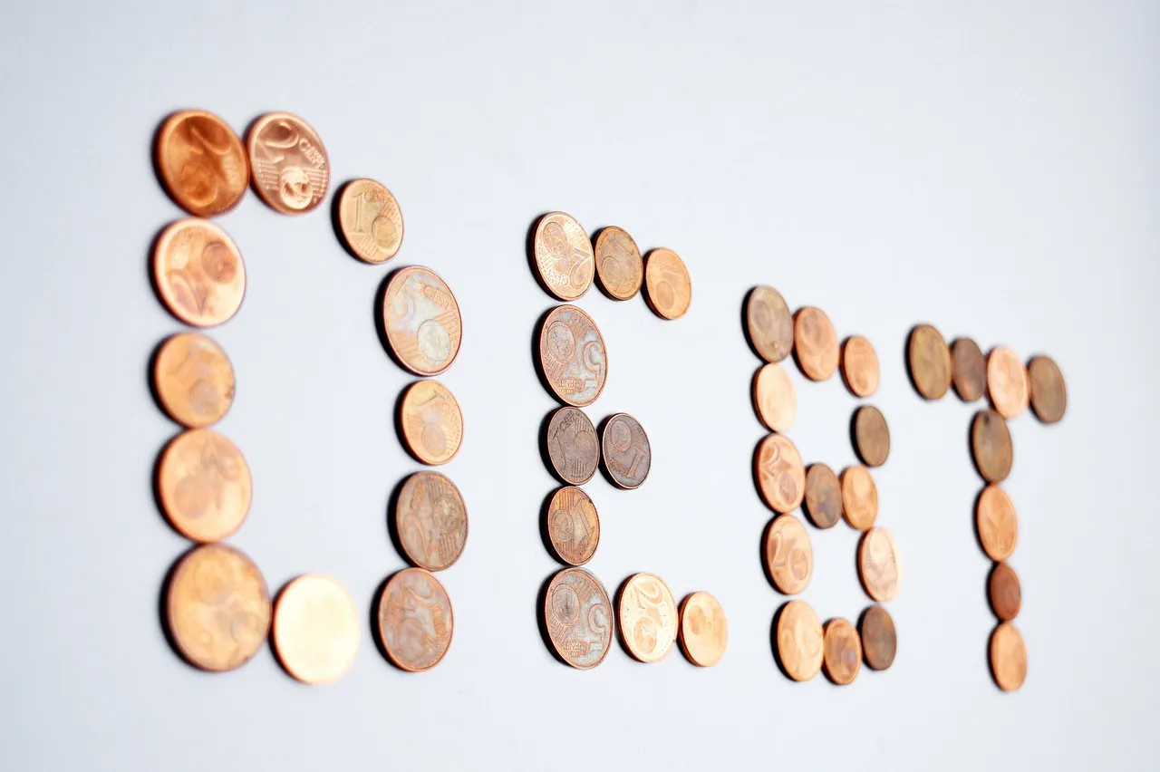 Coins arranged to spell the word "DEBT" on a light background.