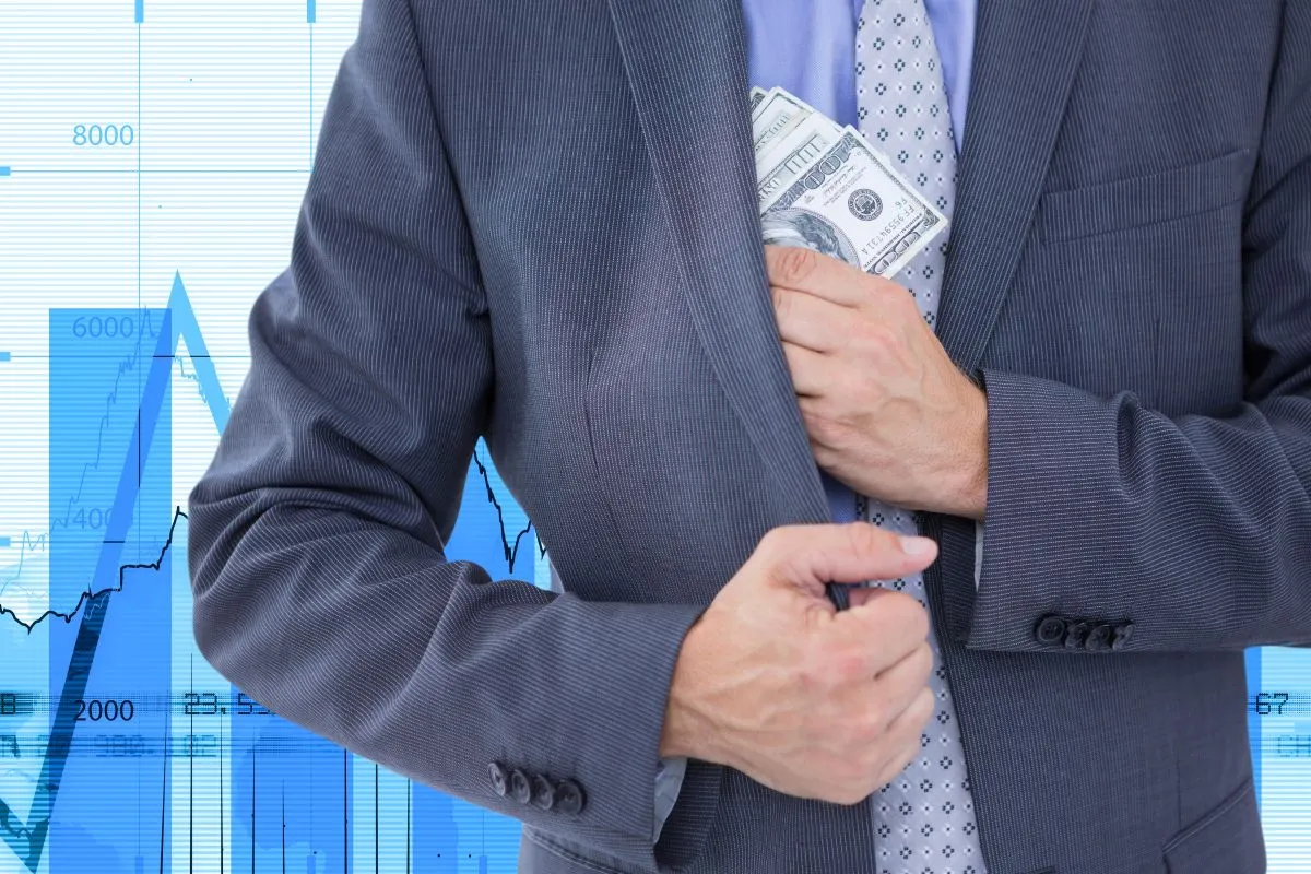 Businessman discreetly placing cash in his suit pocket with financial graphs in the background.