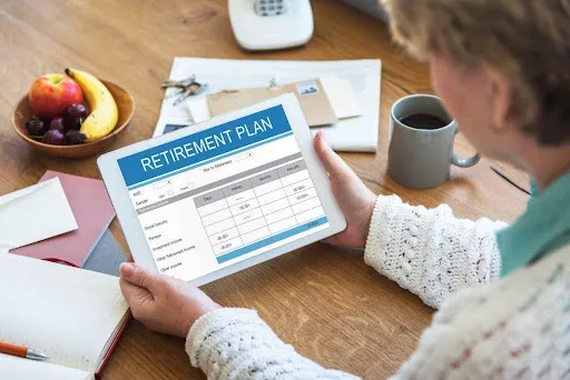 Woman reviewing a retirement plan on a tablet at a desk with coffee and fruit.
