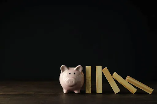 Piggy bank beside toppled wooden blocks on a dark background, symbolizing financial instability.