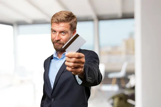 Businessman confidently presenting a credit card in a modern office setting.