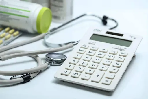 Calculator and stethoscope on a table with medication bottles, symbolizing healthcare budgeting.
