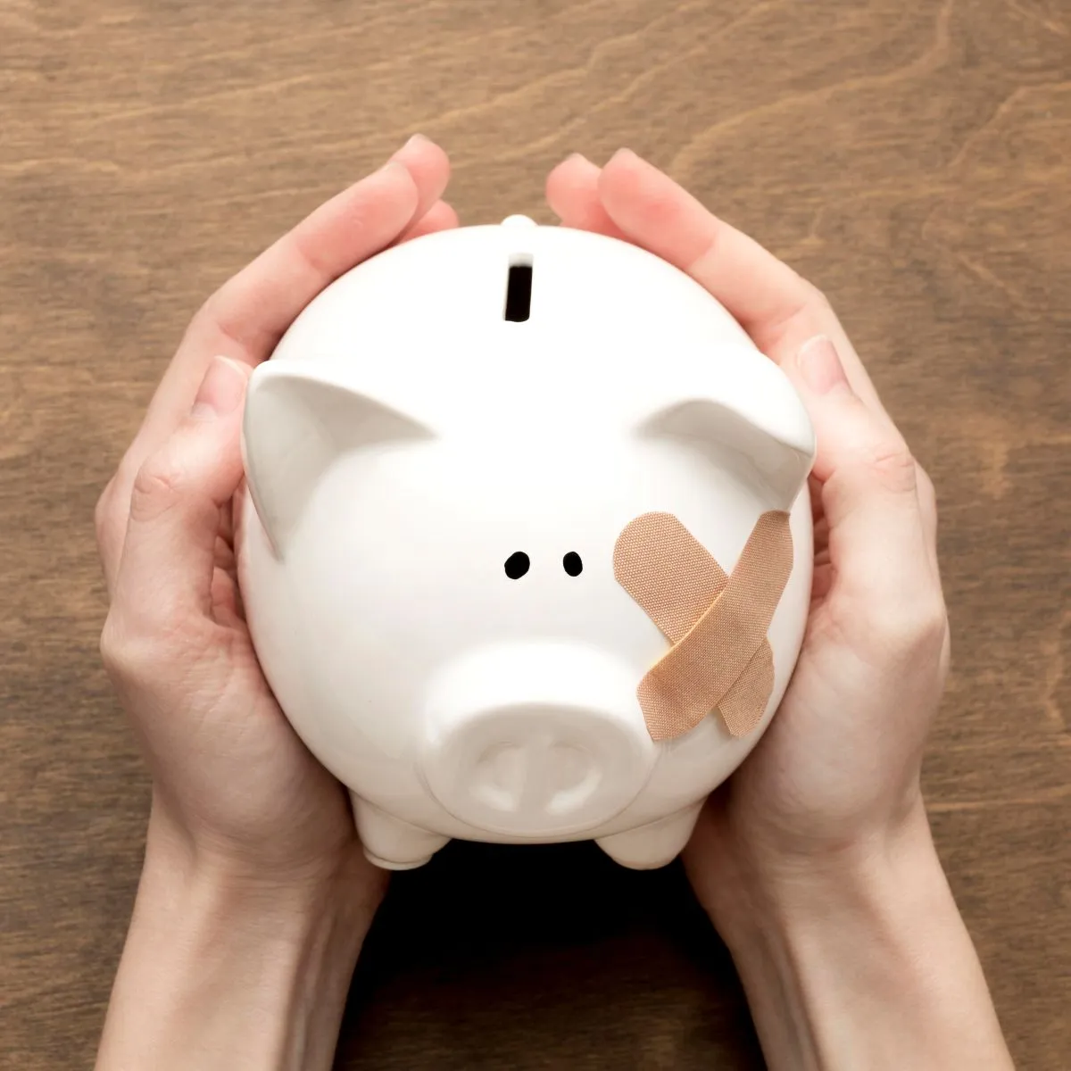 Hands holding a white piggy bank with a bandage, symbolizing saving and financial care.