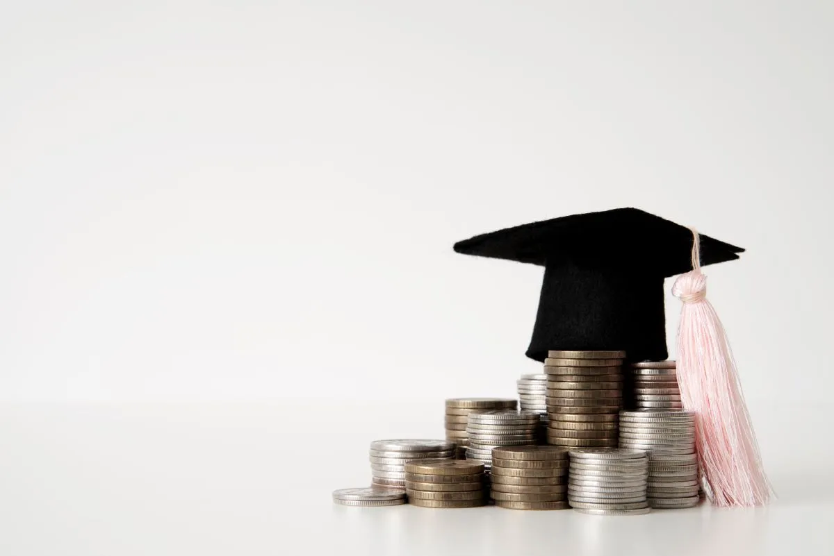 Graduation cap on a stack of coins symbolizing education investment and student debt.