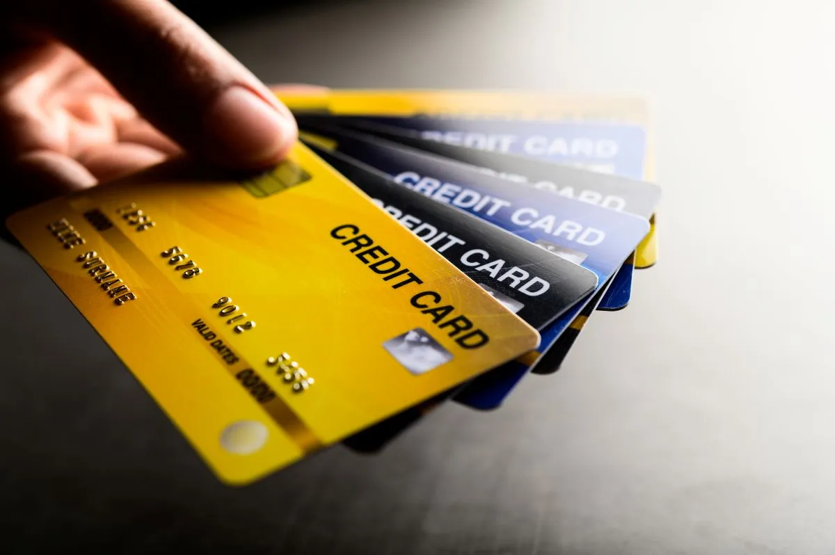 Hand holding multiple credit cards, showcasing various designs and colors on a dark surface.