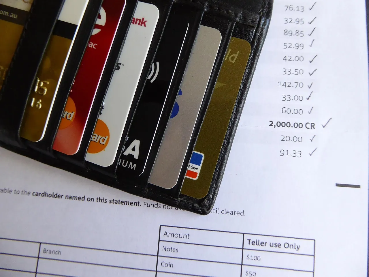 Tarjetas de crédito en una billetera junto a un estado de cuenta bancario que muestra un saldo de crédito.