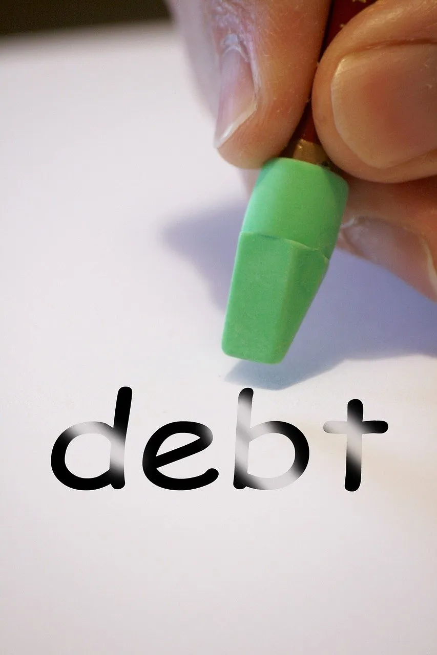 Hand erasing the word "debt" with a green eraser on white paper.