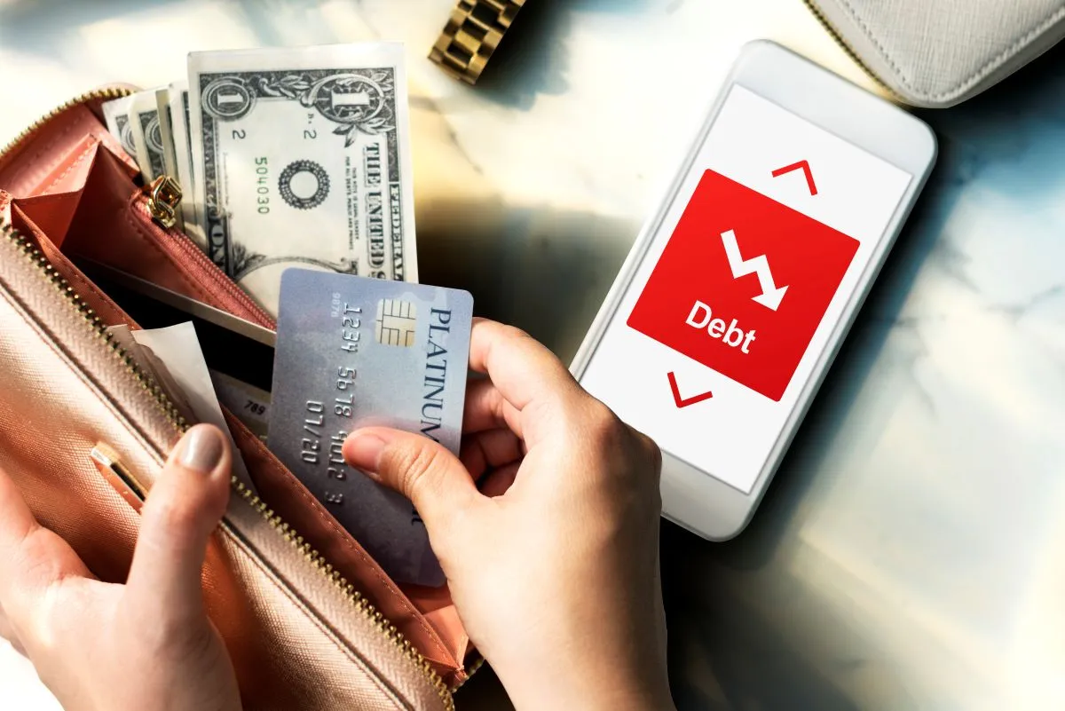 Hands pulling a credit card from a wallet next to a smartphone displaying a debt reduction app.