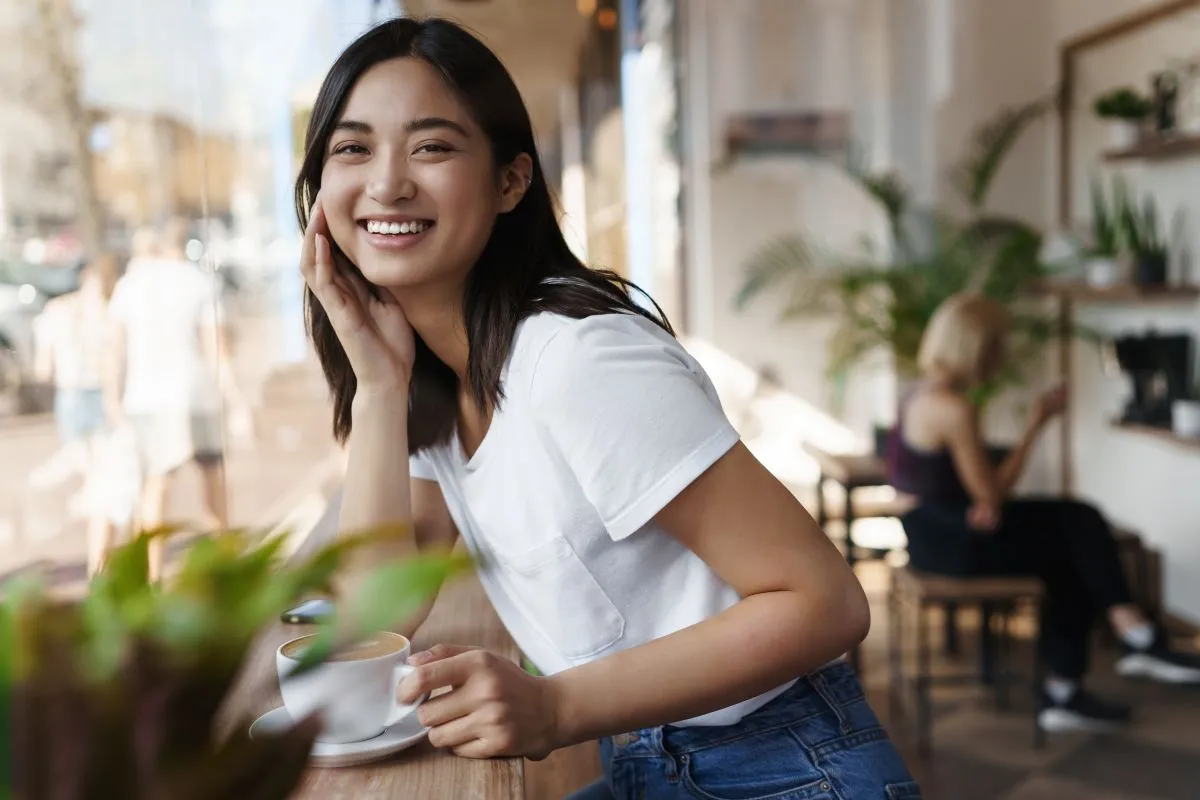 Smiling woman enjoying coffee in a cozy café setting with plants and natural light.