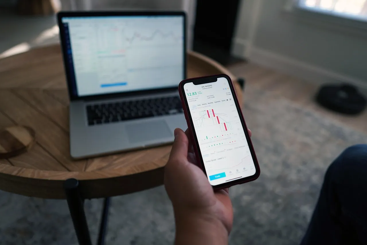 Mobile phone displaying stock market chart with laptop in background.