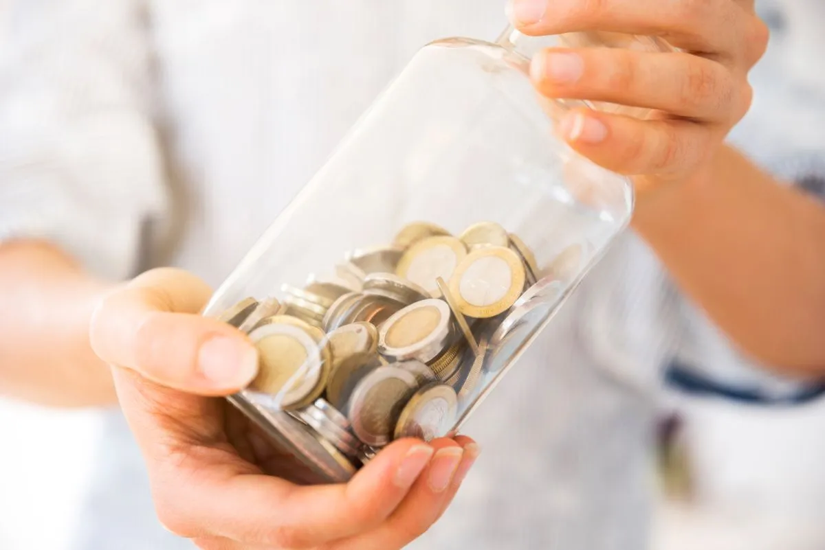 Person holding a glass jar filled with coins, symbolizing savings and financial planning.