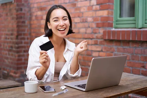Cheerful woman holding a credit card while working on a laptop at a café.
