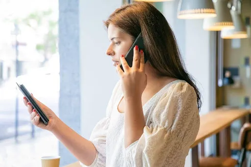 Woman in a cafe talking on the phone while checking her smartphone.