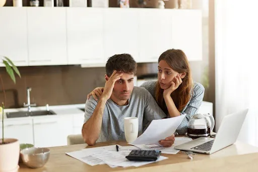 Couple looking stressed while reviewing bills and finances at home.