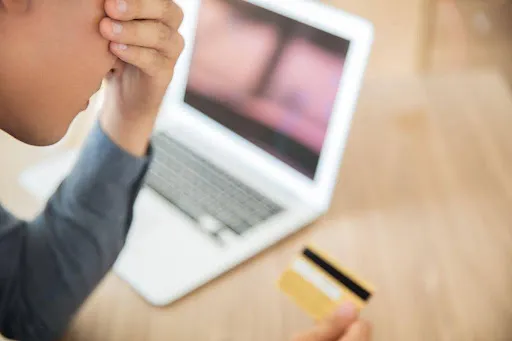 Frustrated person holding a credit card while staring at a laptop screen.