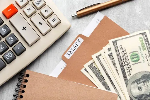 Calculator, cash, and salary folder on a desk, representing financial planning.