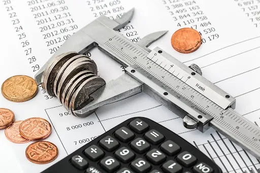 Caliper measuring coins on financial documents with a calculator, symbolizing budgeting and financial analysis.